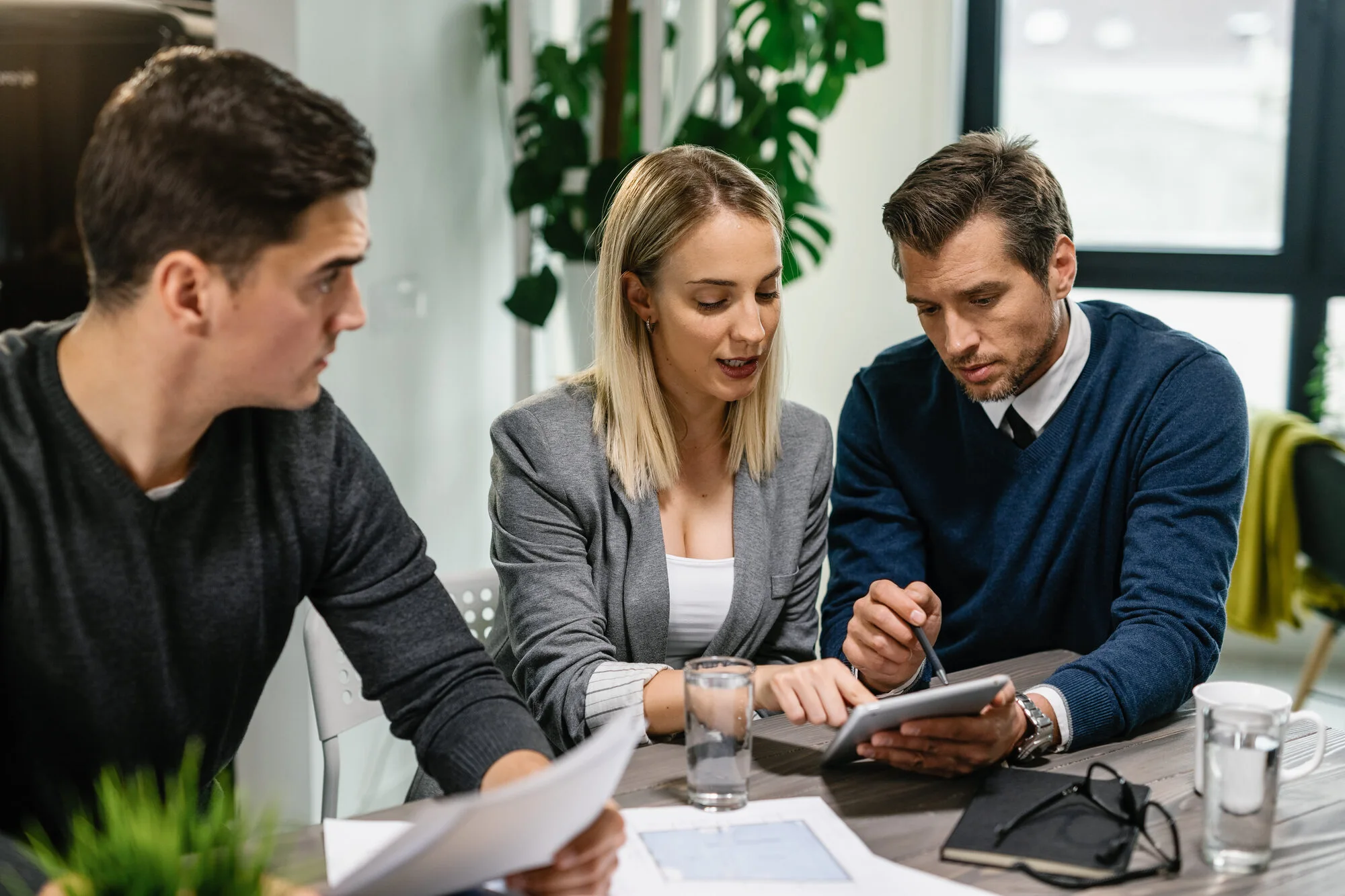 rear-estate-agent-young-couple-going-through-housing-plans-touchpad-while-having-meeting-home