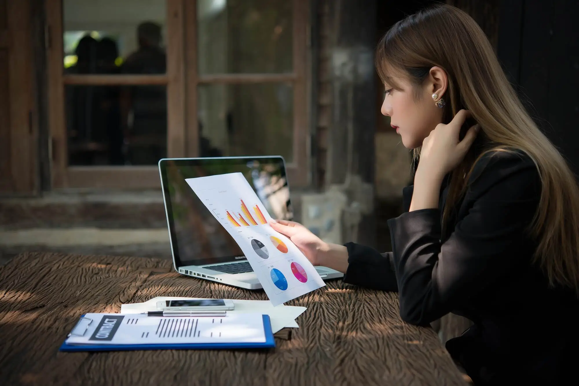 A woman sits at a rustic wooden table, analyzing printed charts with colorful graphs