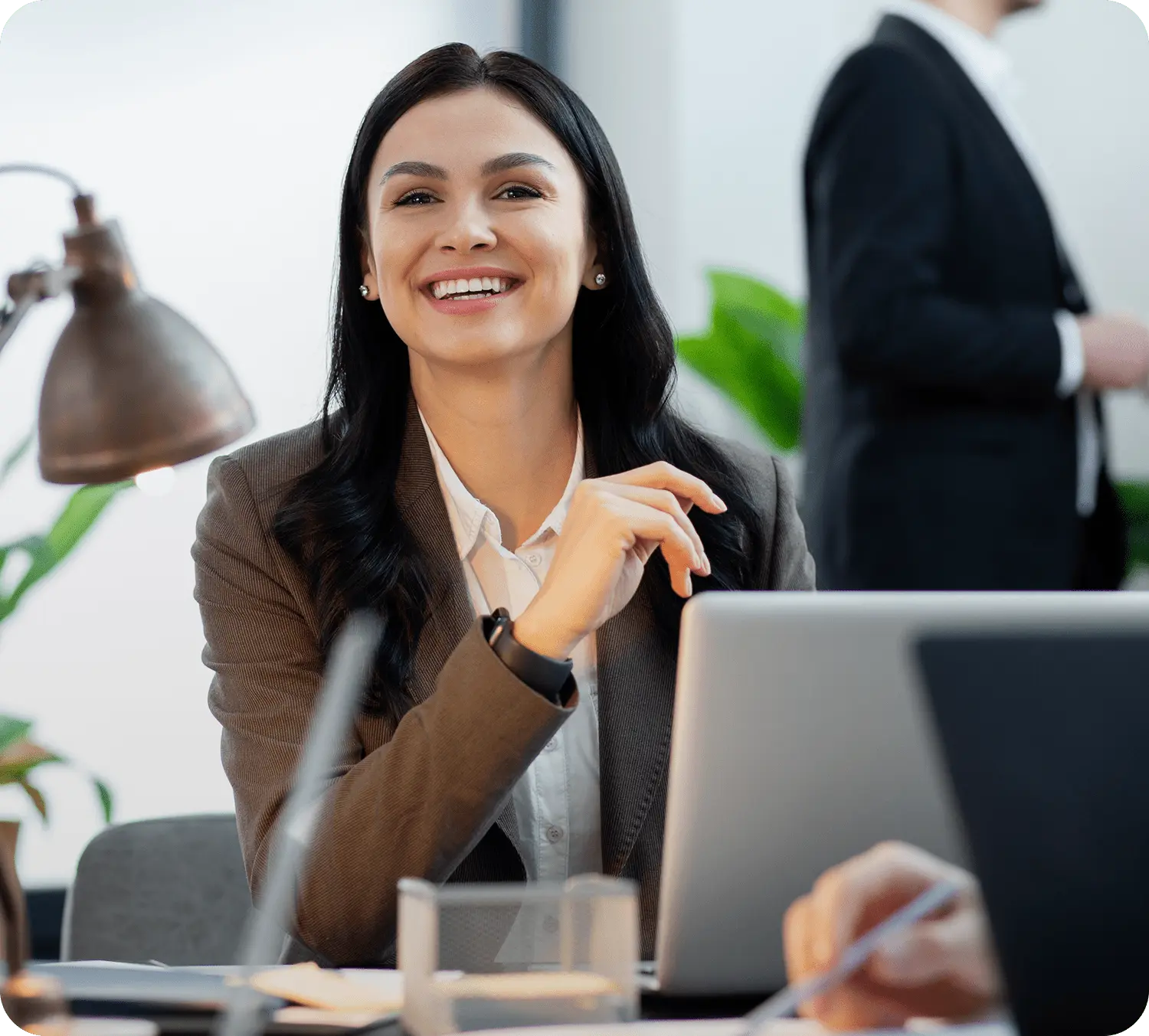 Smiling woman in a business suit sits at a desk with a laptop, exuding confidence