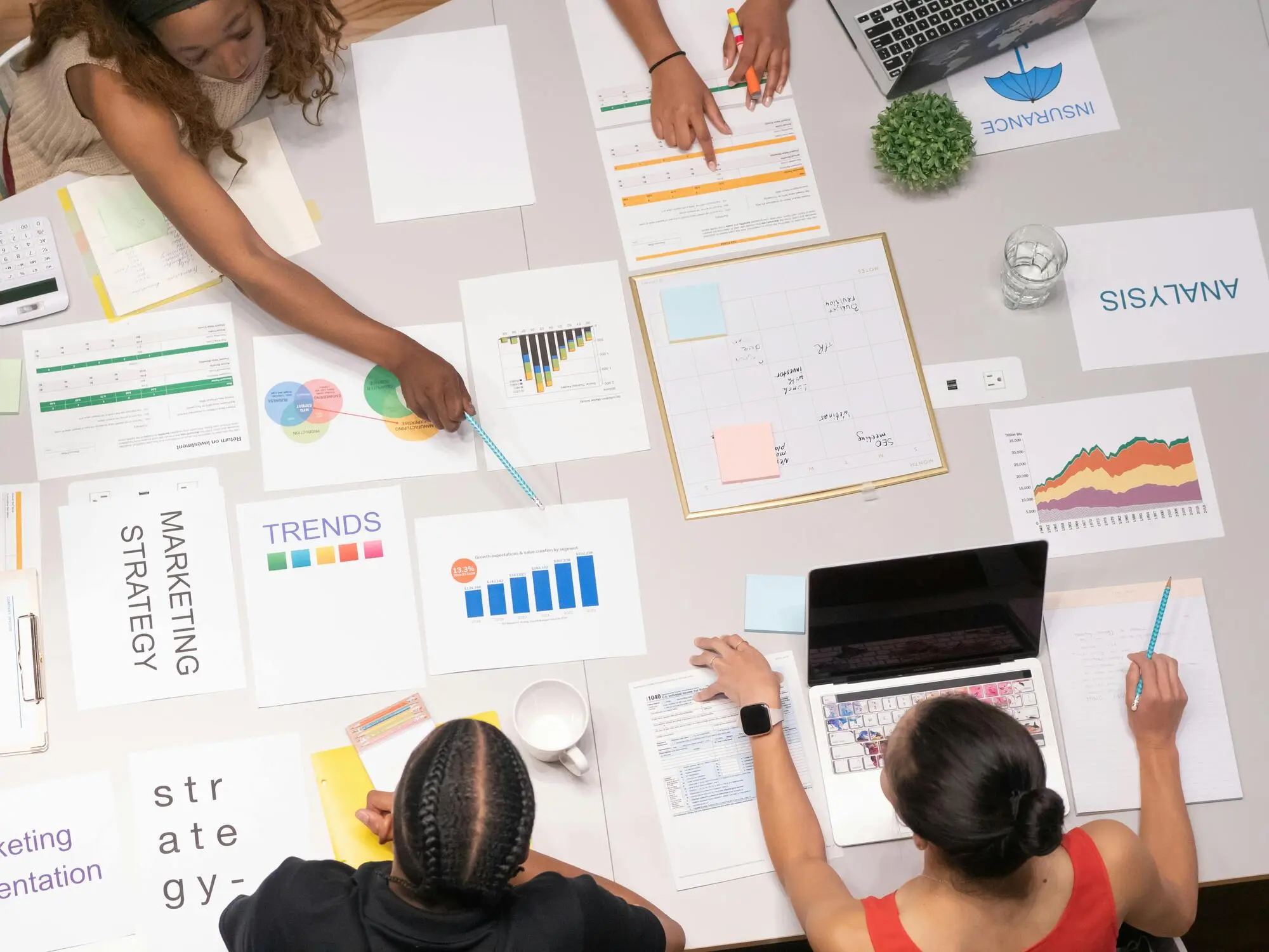 Overhead view of a diverse team collaborating at a desk with charts, graphs, and laptops, focusing on marketing strategies and data analysis, conveying teamwork